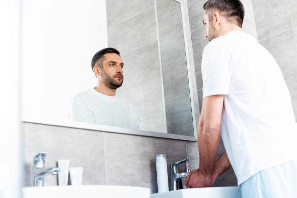 istock handsome man looking in mirror and washing hands in bathroom during morning routine 1155240517