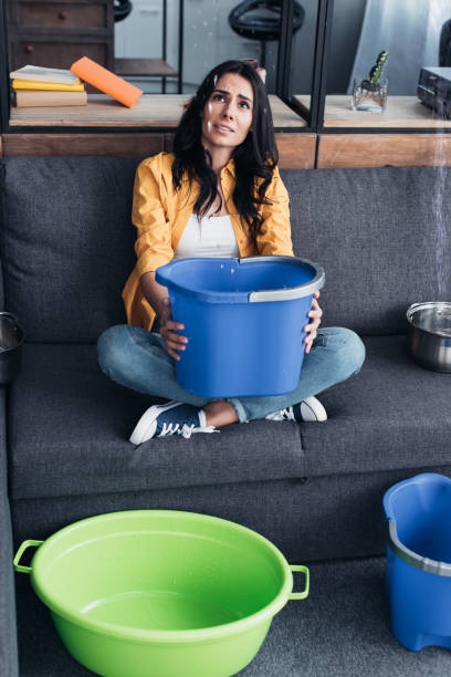 istock Upset woman with buckets and basin looking at leaking ceiling 1155242513
