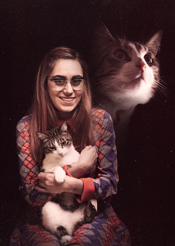 A vintage styled photograph of a woman posing for a portrait with her cat, a profile view of the cat superimposed at the top of the image.