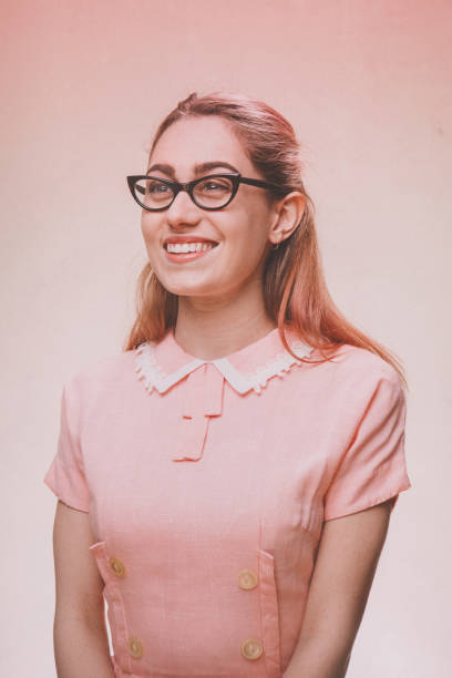 Retro Stereotypical Nineteen Fifties Portrait of Fashionable Woman A 1950's styled young woman in a vintage pink dress and cats eye glasses.  Pink background. high school photos stock pictures, royalty-free photos & images