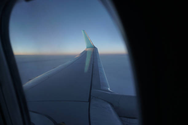istock Airplane window overlooking the beautiful clouds and the earth. Sunset in flight on vacation. Tourist theme. Stock photo 1155250525