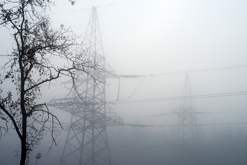 High-voltage electric tower in the fog against the background of the forest.