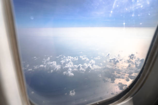 Airplane window overlooking the beautiful clouds and the earth. Sunset in flight on vacation. Tourist theme. Stock photo