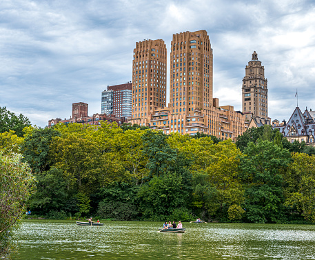 Central Park Lake and West Side skyline, New York City.People gather together on strawberry fields, people rowing on the lake.