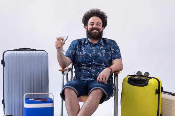 voyageur de hipster joyeux se reposant dans sa chaise buvant sa boisson préférée - travel suitcase hawaiian shirt people traveling photos et images de collection