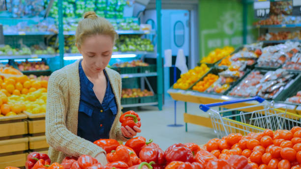 mulher que compra pimentas de sino vermelhas frescas na mercearia - pepper bell pepper market spice - fotografias e filmes do acervo