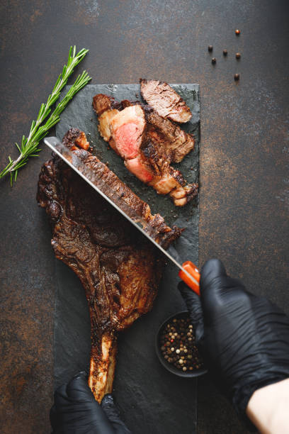 istock Man in black gloves cuts grilled marble beef steak Tomahawk. Top view, dinner concept. 1155277004