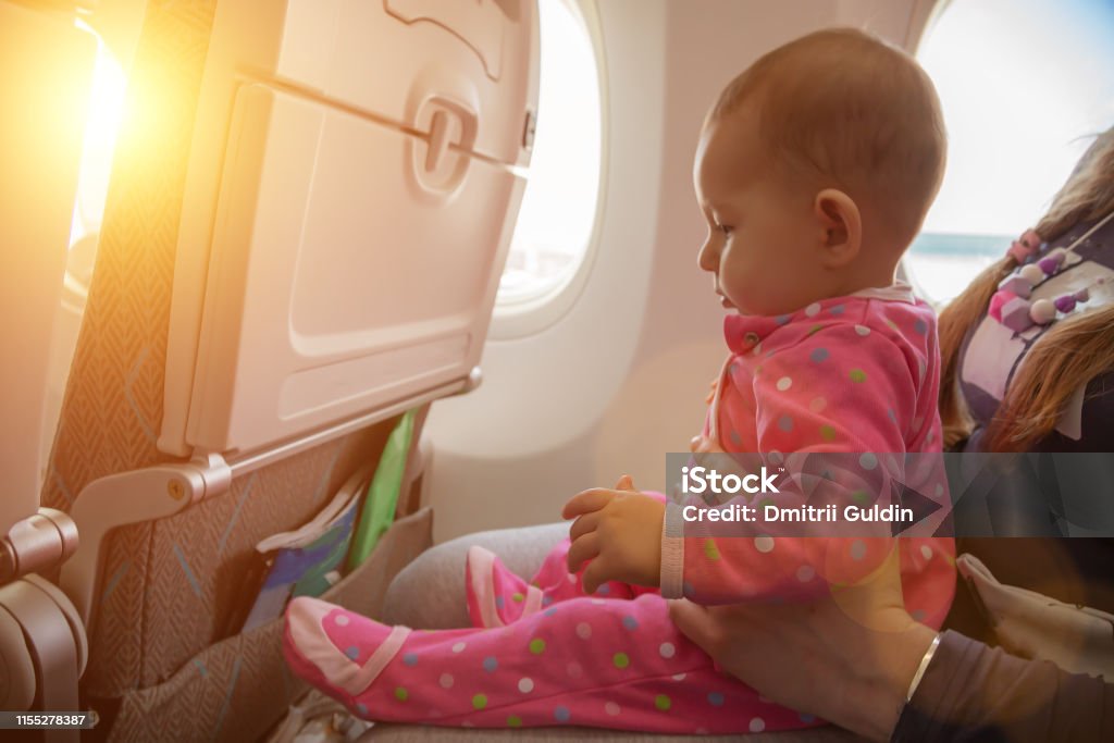 Travelling with infant. Mother and baby sitting together in airplane near the window in sunny day Baby - Human Age Stock Photo