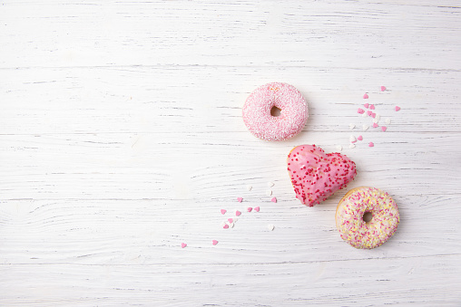 Tasty fresh donuts in a shape of the heart on a wooden background, top view