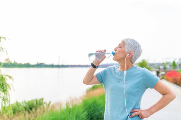 spragniona kobieta jogger picia świeżej wody i słuchanie muzyki w słuchawkach po treningu - water bottle sports and fitness selective focus sport zdjęcia i obrazy z banku zdjęć