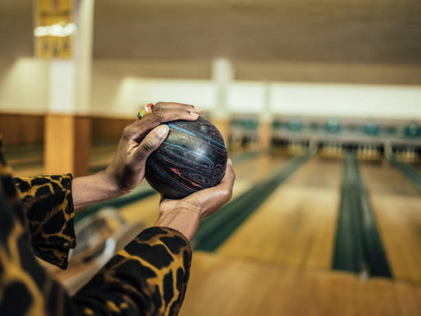 Close up of hands of African millennial woman getting ready to roll the bowling ball, concentrating at the edge of bowling alley.