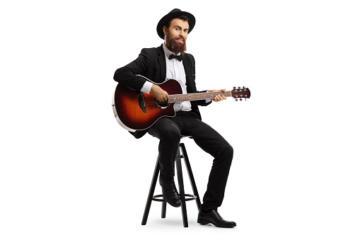 Full length shot of a male musician sitting and playing an acoustic guitar isolated on white background
