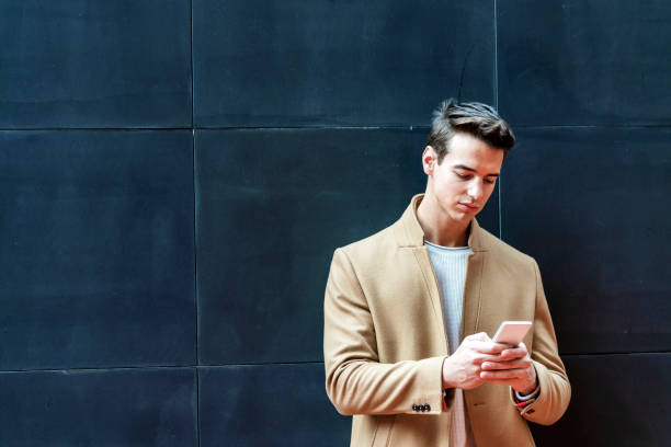 istock Young man writing phone message. Mid adult man typing on mobile while standing on grey background. 1155292290