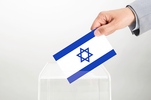 Human hand is inserting Israel flag into ballot box. Representing voting in Israel.