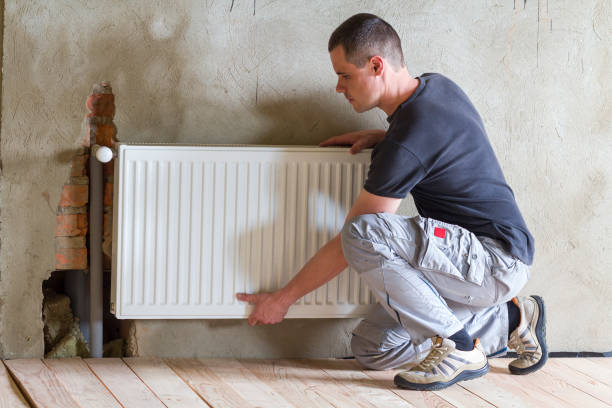 istock Young handsome professional plumber worker installing heating radiator in an empty room of a newly built apartment or house. Construction, maintenance and repair concept. 1155293466