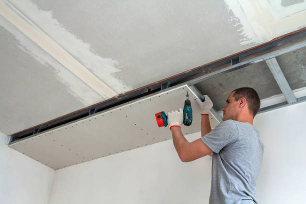 young man in usual clothing and work gloves fixing drywall suspended ceiling to metal frame using electrical screwdriver on ceiling insulated with shiny aluminum foil. diy, do it yourself concept. - ceiling imagens e fotografias de stock