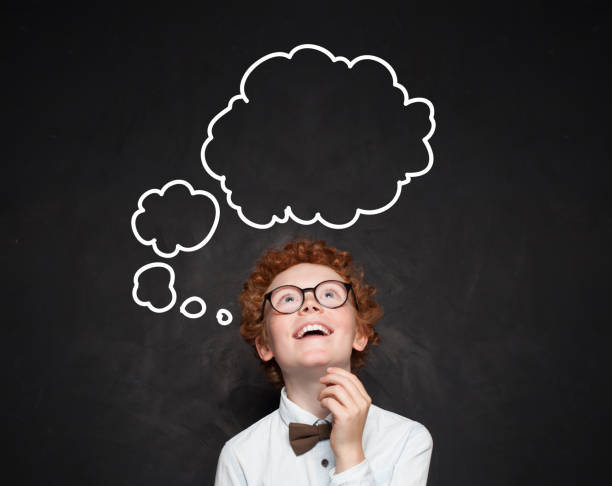 istock Happy smart kid with empty speech clouds bubbles at the classroom blackboard. Education and school concept. Student boy portrait 1155294384