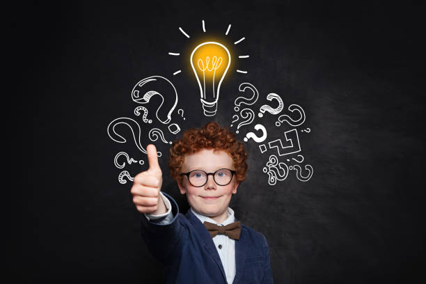 istock Smart boy student showing thumb up on blackboard background with lightbulb and question mark. Brainstorming and idea concept 1155294408