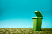Green recycle bin on green grass and blue sky