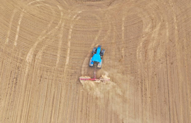istock Aerial top down view on blue tractor pulling a plow, preparing a soil for seed sowing, tractor making dirt cloud. 1155302411