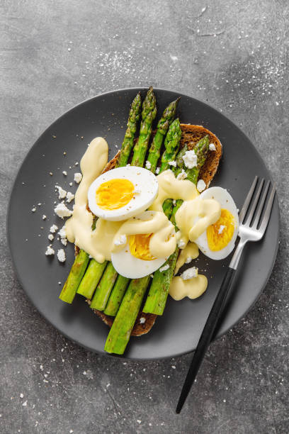 Tasty toasts with asparagus, eggs and sauce Tasty appetizing toast with asparagus, eggs, cheese and sauce hollandaise served on plate on grey background. View from above with copy space. hollandaise sauce stock pictures, royalty-free photos & images