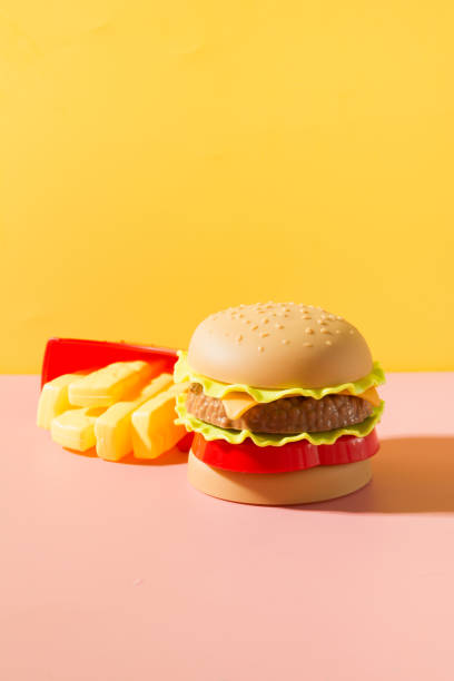 istock Plastic burger, salad, tomato, frying potato with on yellow. 1155305400