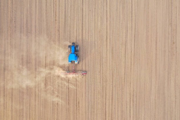 istock Aerial top down view on blue tractor pulling a plow, preparing a soil for seed sowing, tractor making dirt cloud 1155305515