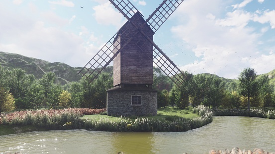 Traditional village windmill standing near the pond against the background of mountains and clouds. Beautiful nature and Summer landscape.