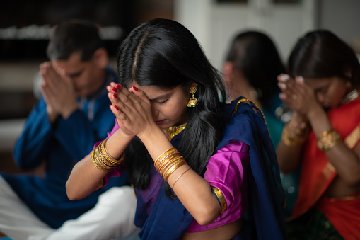 Una hermosa familia India se sienta en su sala de estar una tarde orando juntos. Están celebrando y dando gracias durante las vacaciones Diwali. Se están uniendo a medida que se donan en la ropa tradicional. photo
