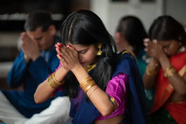 Photo of A beautiful Indian family sits in their living room one afternoon praying together. They are celebrating and giving thanks during the holiday Diwali. They are bonding as they are donned in traditional clothing.