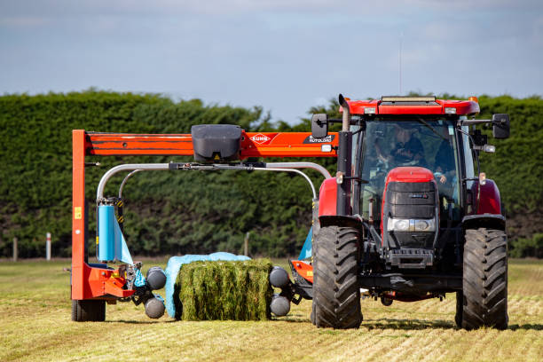 A bale wrapper attached to a farm tractor wraps hay bales for winter stock food Kirwee, Canterbury, New Zealand, March 27 2019: A demonstration of a hay bale wrapper at work at the South Island Agricultural Field Days event hay baler stock pictures, royalty-free photos & images
