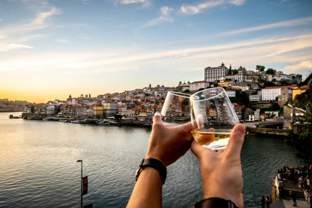 Couple toasting with the Douro river and Porto in background at sunset. Personal perspective (POV) of a couple toasting a wine glass in the foreground of a scenic view in Porto.  Blue skies and soft white clouds roam over the Douro river between the cities of Porto and Vila Nova de Gaia display it's colourful City-line in the background. portuguese culture photos stock pictures, royalty-free photos & images