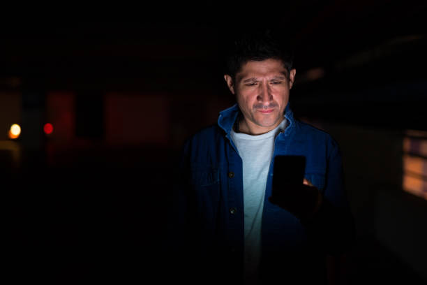 istock Suspicious-looking Hispanic man using phone in dark parking lot 1155331086