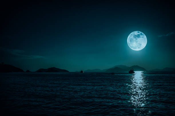Scenic view of small boat in calm sea water at night time and super moon. serenity nature background. stock photo