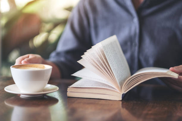 istock a woman holding and reading a book while drinking coffee 1155341599