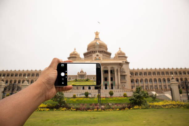 mains montrant de prendre une photo de vidhana soudha avec le téléphone portable. - mobilestock photos et images de collection