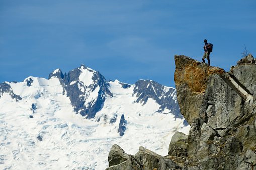 Mid distance view of hiker standing on mountain. Male backpacker is looking at snowy landscape. He is exploring nature against sky.