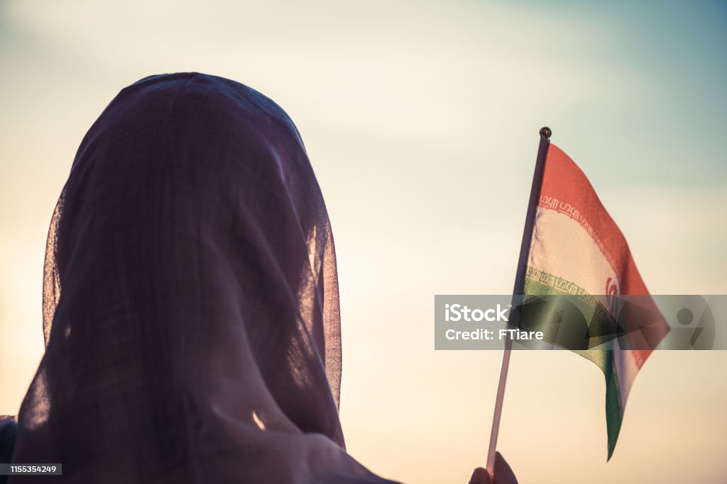 Muslim woman in scarf with Iranian flag at sunset.Concept Iran Stock Photo