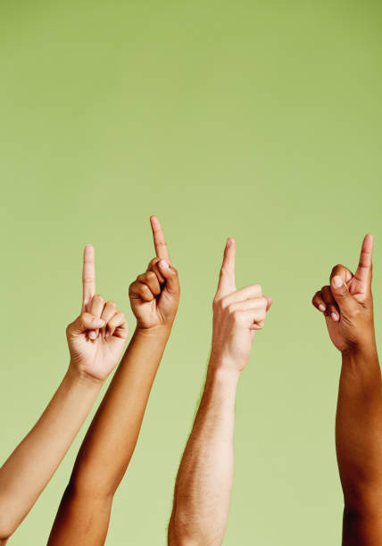istock Four mixed hands point upwards against green 1155361086