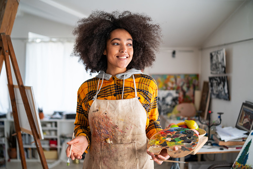 Smiling young afro woman holding color palette and paintbrush