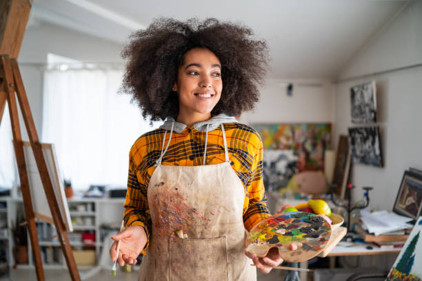 Smiling young afro woman holding color palette and paintbrush Smiling young afro woman holding color palette and paintbrush workshop art studio art paint stock pictures, royalty-free photos & images