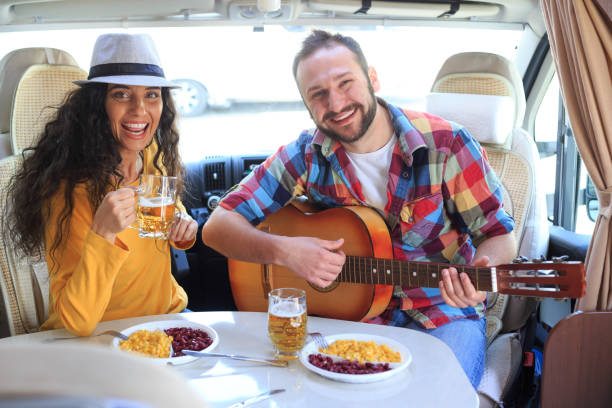 Couple enjoying trip with camper, drinking beer and playing a guitar.