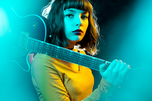 Hermosa joven hipster mujer con pelo rizado con guitarra roja en luces de neón. Rock músico está tocando guitarra eléctrica. concepto de estilo de los 90. photo
