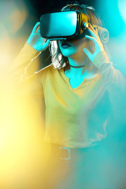 joven hipster mujer con pelo rizado que lleva gafas de realidad virtual y toca otro mundo en luces de neón de estudio. smartphone con casco de rv. - vertical caucasian glasses red hair fotografías e imágenes de stock