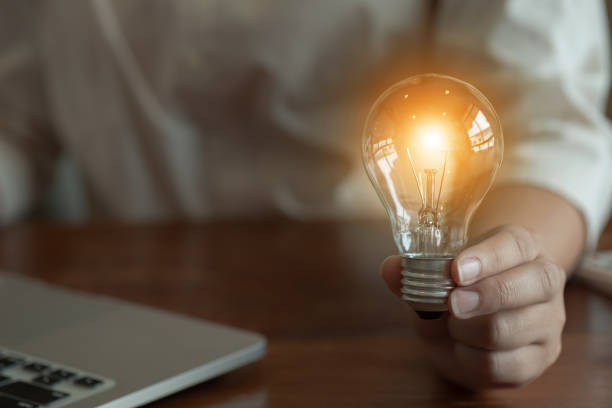 istock woman hands holding light bulb in working place. 1155372300