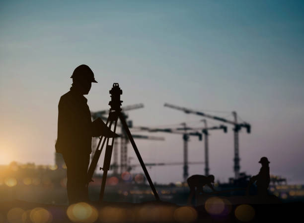 ingegnere di silhouette cercando caricatori e camion in un cantiere sopra operaio edile sfocato in cantiere - perito foto e immagini stock