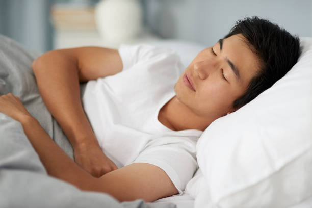 Cropped shot of a handsome young man sleeping under a duvet in his bed in the morning