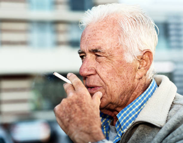 istock Senior man smoking cigarette outside building 1155376498