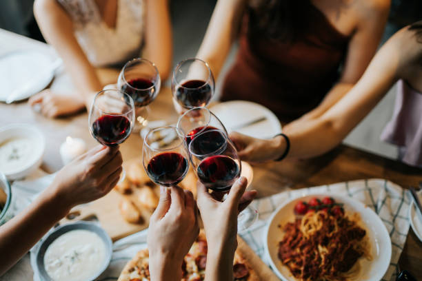 楽しさと乾杯を持つ幸せな若い友人のクローズアップとパーティー中に赤ワインで祝う - ワイン ストックフォトと画像