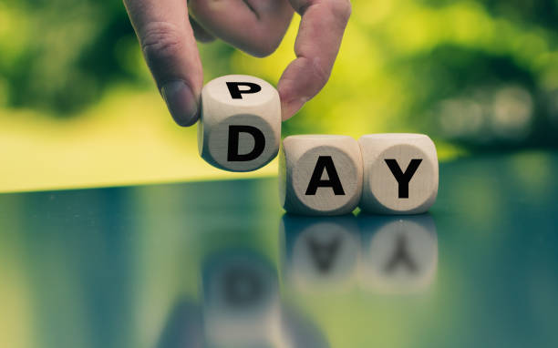 Hand is turning a dice and changes the word Pay to Day. stock photo